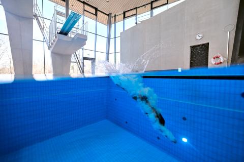 Frau springt von Sprungturm und taucht ins Wasser ein