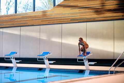 Schwimmerin in der Hocke auf Startblock im Schwaketenbad